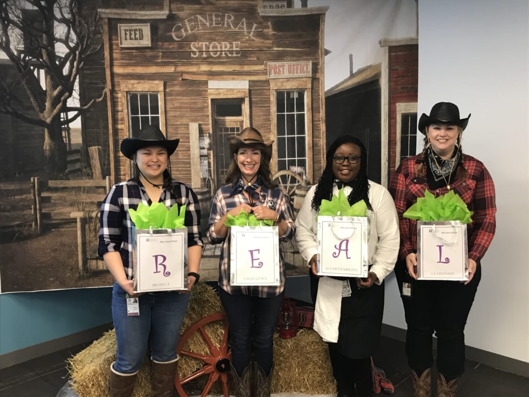 Four people in western costumes holding letters that make up REAL
