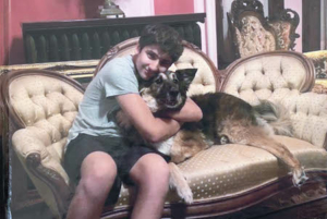 Delfs_Rocky_2023_Featured_450x300 Photograph of Rocky Delfs sitting on a couch, hugging a dog and smiling into the camera.
