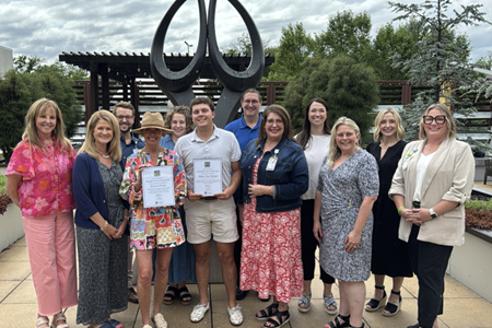 A group of men and women posed in front of a tall sculpture that represents the gift of life through organ donation.