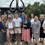 A group of men and women posed in front of a tall sculpture that represents the gift of life through organ donation.